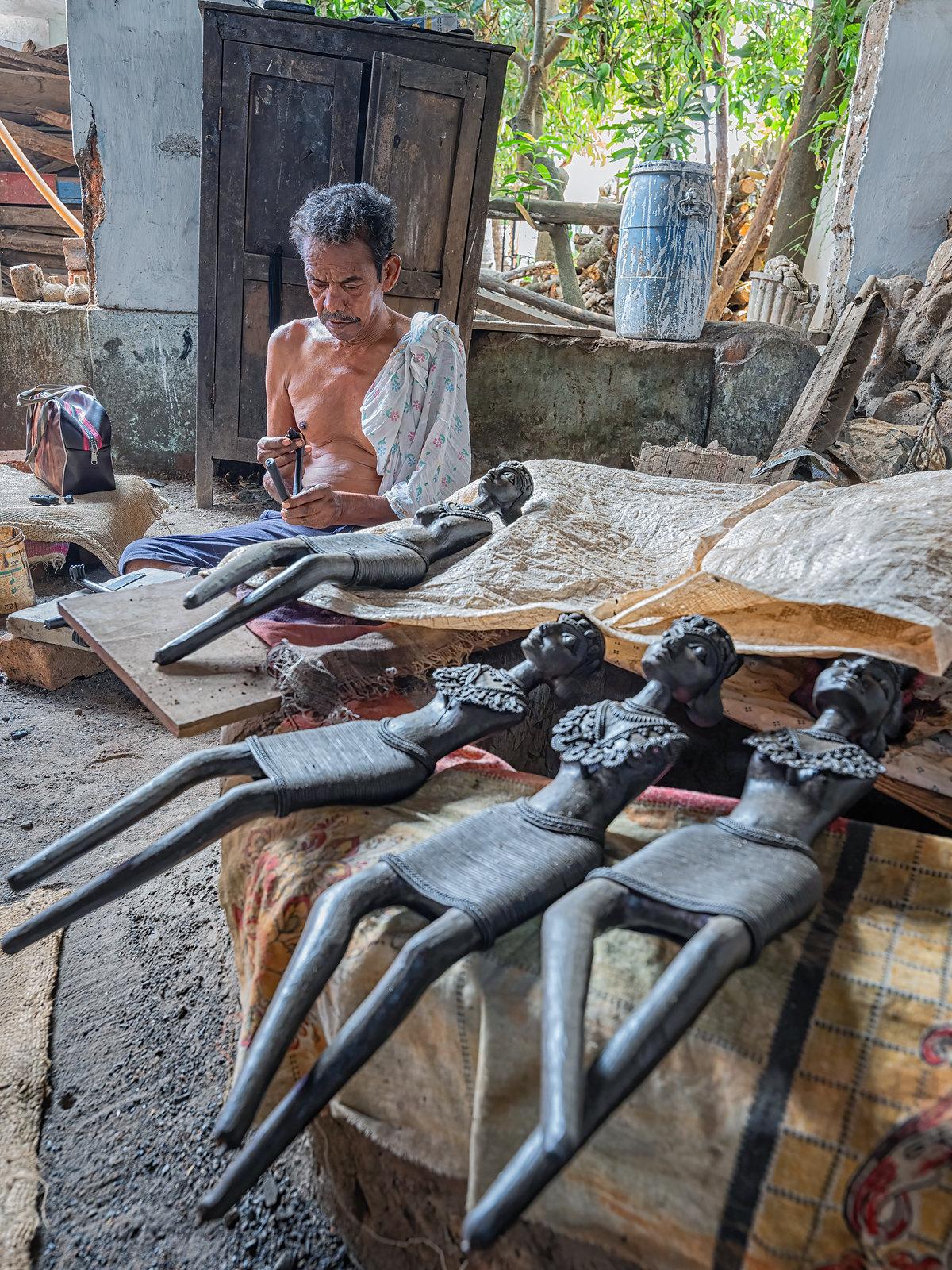 An artisan at work behind a row of wax-wound figures laid out on the ground.