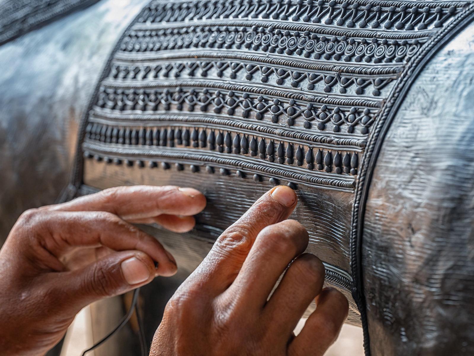 Two hands laying a wax thread against a surface already wound in rows of spirals and beading.