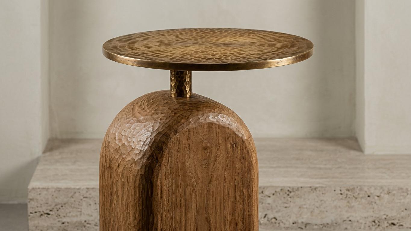 Hand-adzed oak base carrying a hammered brass disc top, on travertine.